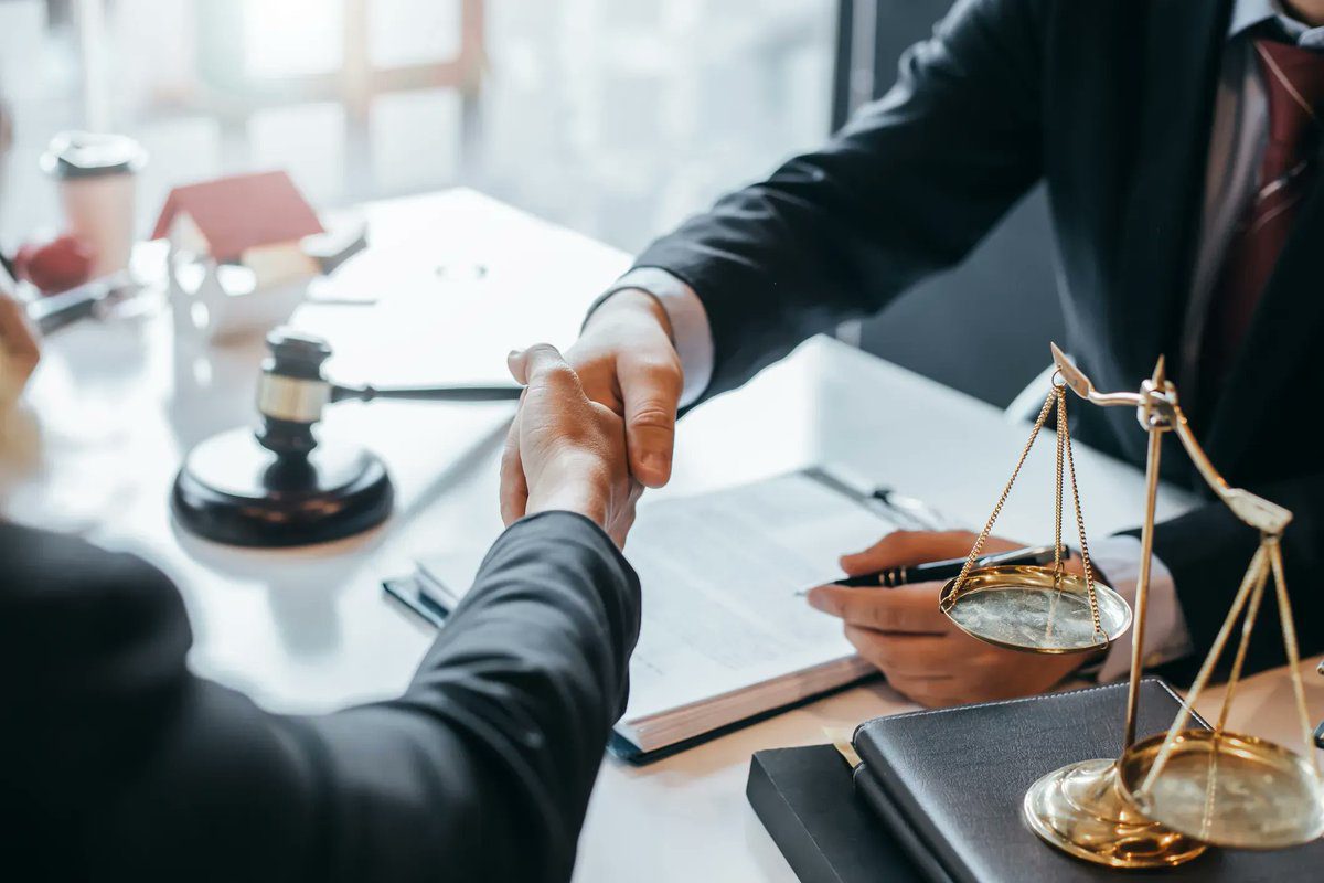 Two people shaking hands over a table with papers and a gavel.