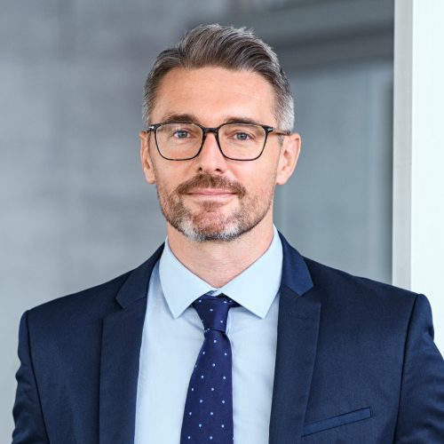 A man in a suit and tie standing next to a wall.