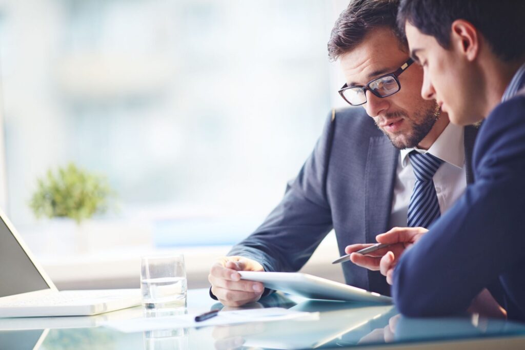 Two men in suits and ties looking at a tablet.