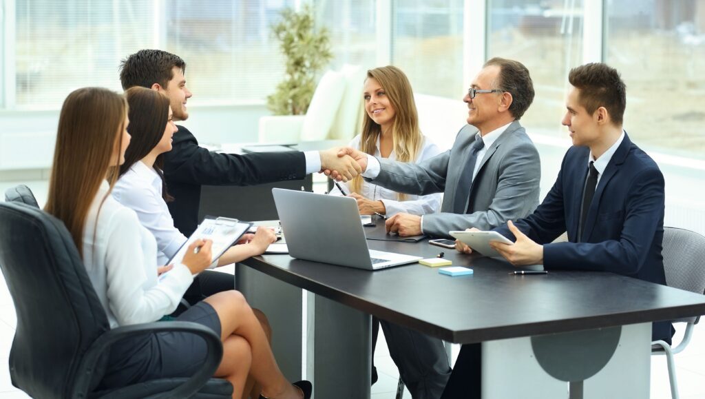 A group of people sitting around a table shaking hands.