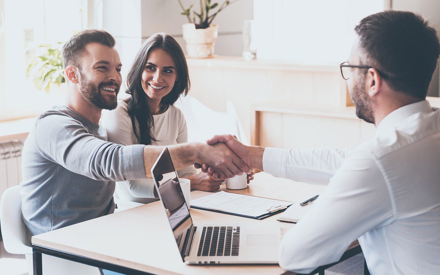 A man and woman shaking hands over a laptop.