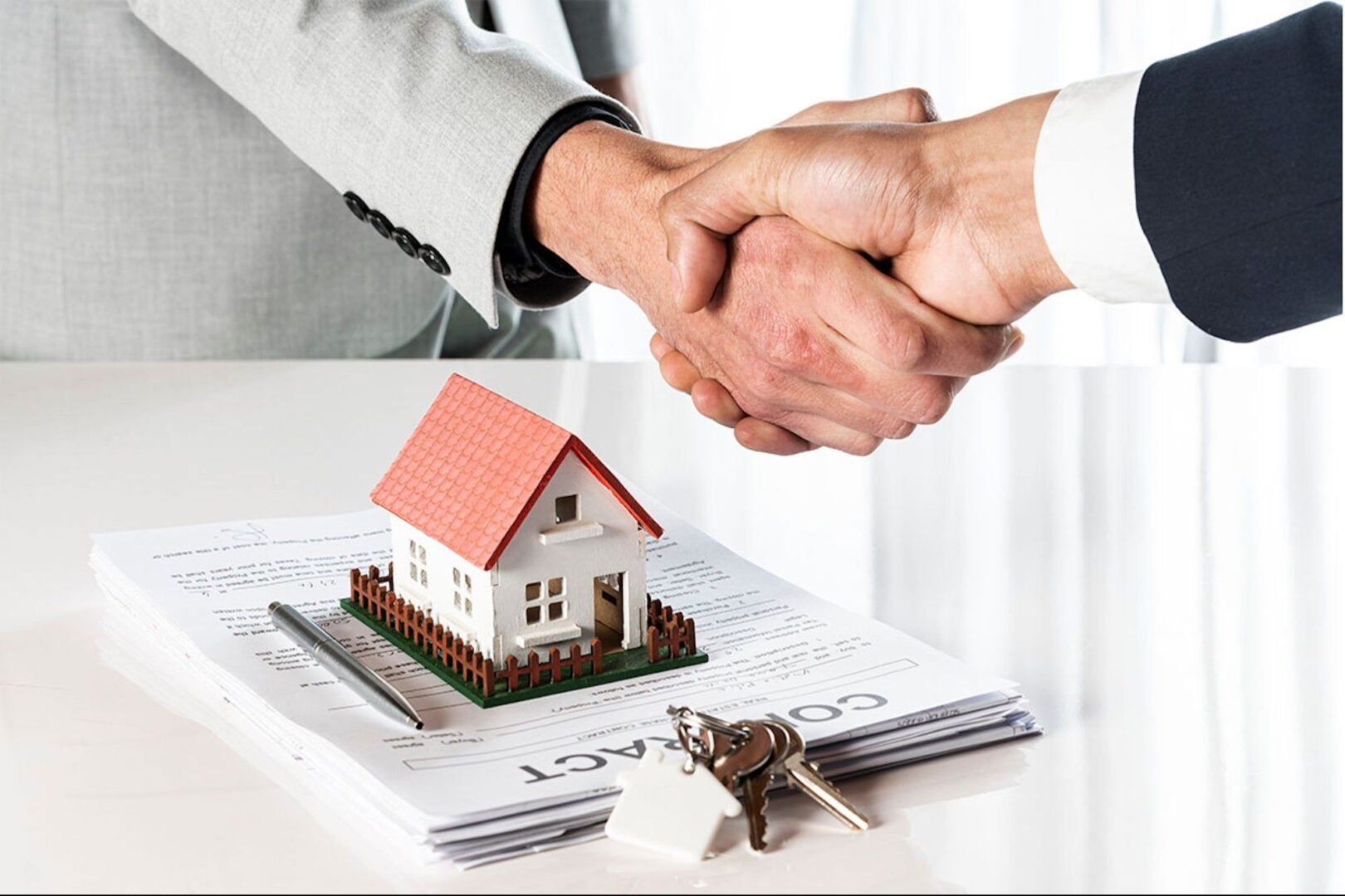 Two people shaking hands over a house with keys.