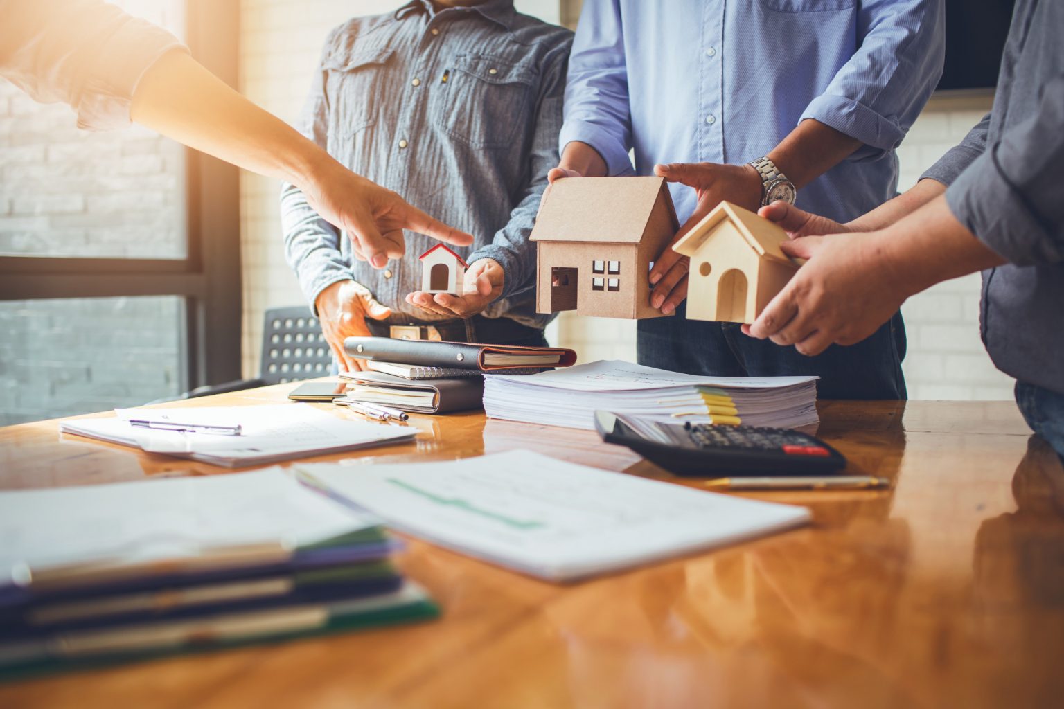 A group of people holding wooden houses on top of papers.