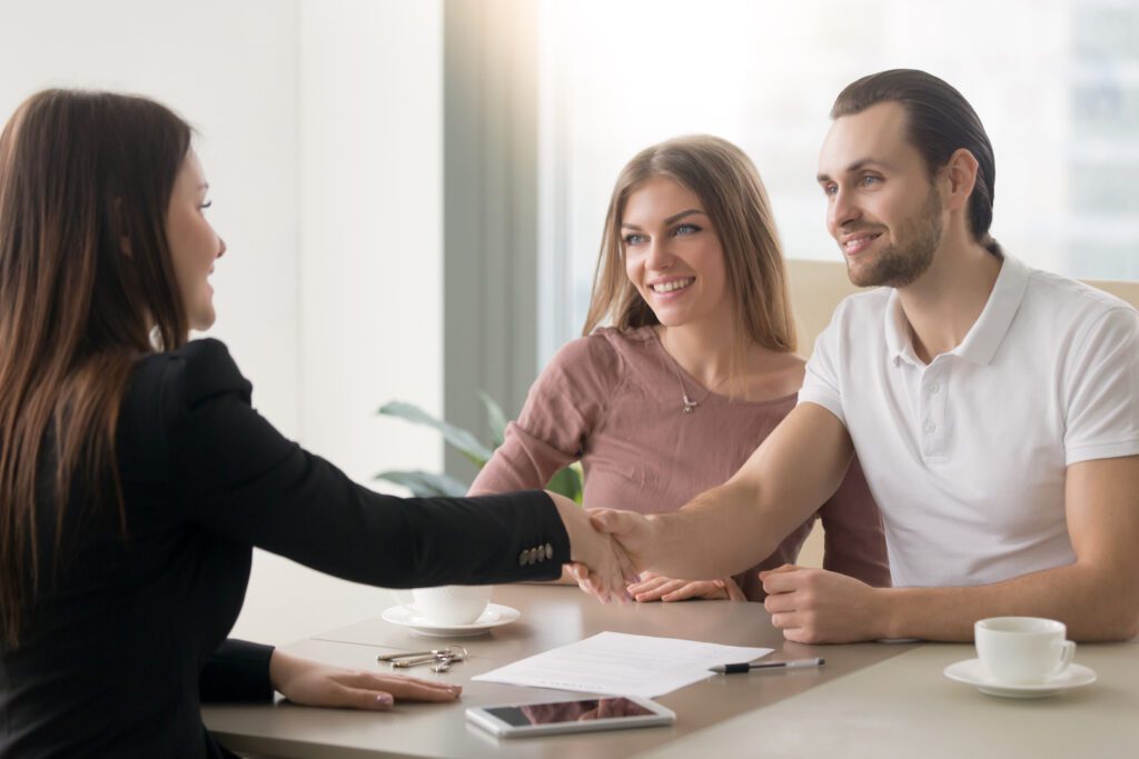 A woman shaking hands with two men in front of a table.